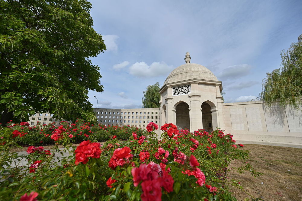 Red flowers bloom in front of one of the stone rotundas at Neuve-Chapelle Indian Forces Memorial