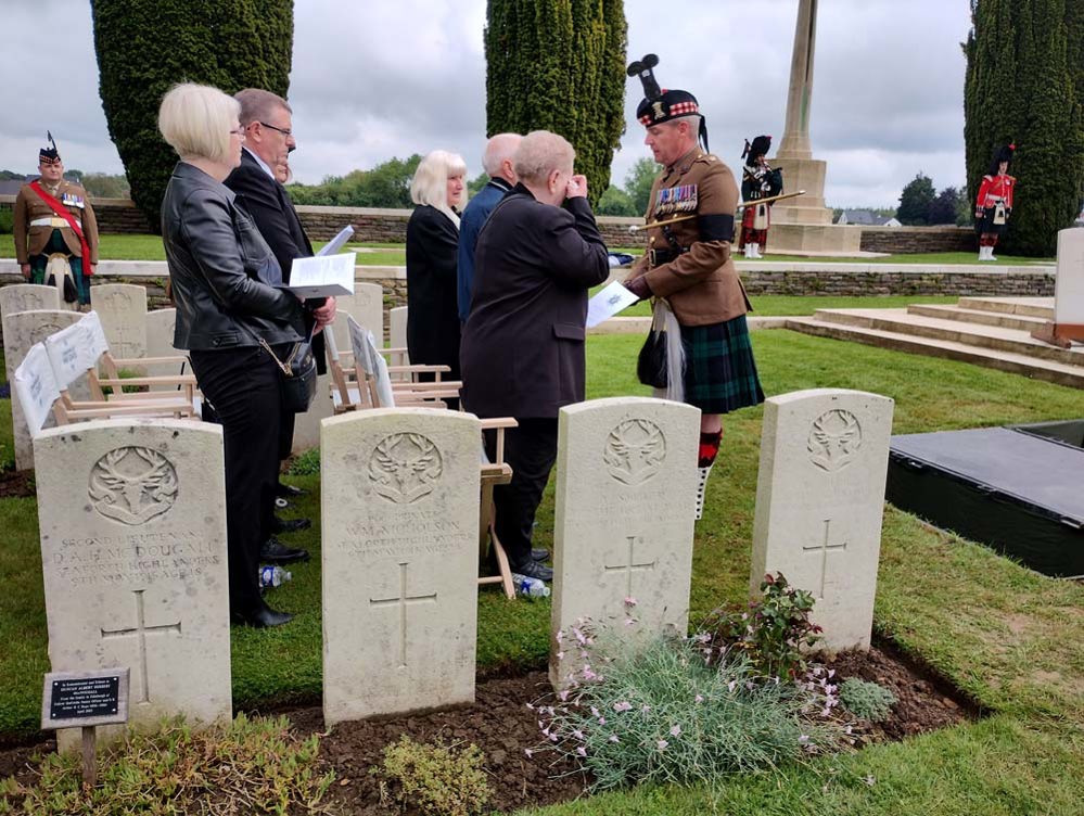 A Scottish soldier in kilt talking with a group of mourners at a rededication ceremony in a CWGC cemetery.