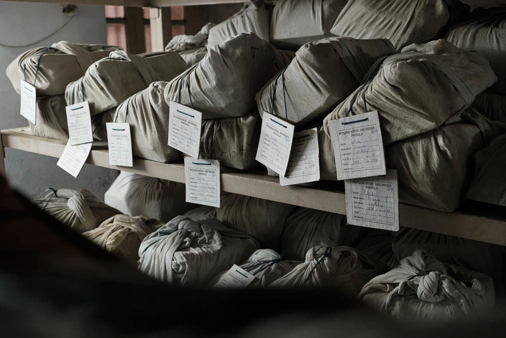 Stacks of old record books and documents wrapped in cloth bags on library shelves