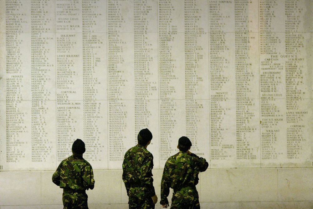 Three soldiers in camo fatigues and berets looking at the name panels inside the Ypres (Menin Gate) Memorial.