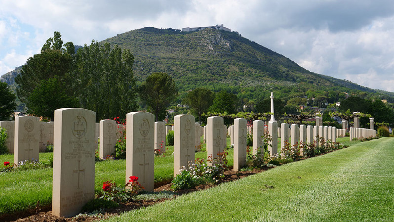 A row of headstones at Cassino War Cemetery with Monte Cassino visible in the background.