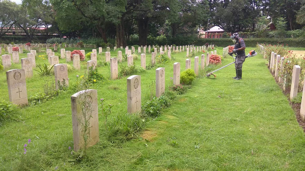 A CWGC gardener uses a strimmer to trim the grass lawn in Ranchi War Cemetery.