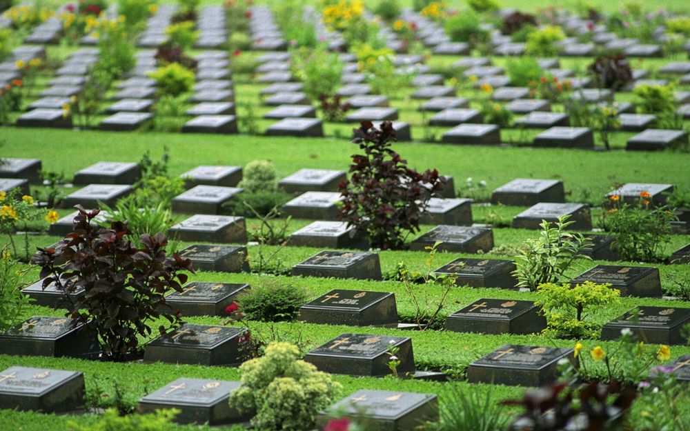 Rows of bronze plaque war grave markers set amidst a lush green lawn at Kanchanaburi War Cemetery.