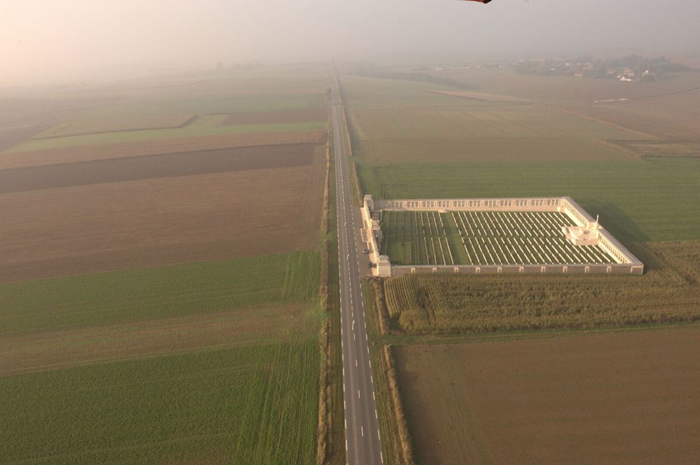 Pozieres British Cemetery as seen from the air. The cemetery sites in farmer fields next to a wide straight road.