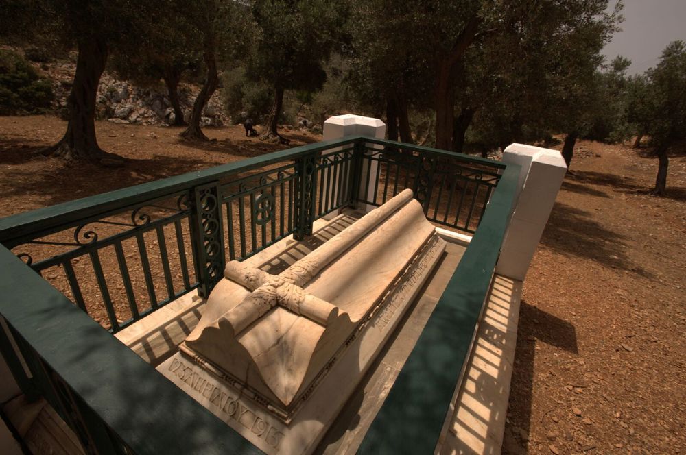 Rupert Brooke's tombe. It is a white stone sarcophogus topped with a cross surrounded by green painted railings on either side.