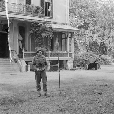 Roy Urquhart poses next to a lance bearing a 1st Airborne Division pendent. The lance has been stuck in the ground outside the Hartenstein Hotel.