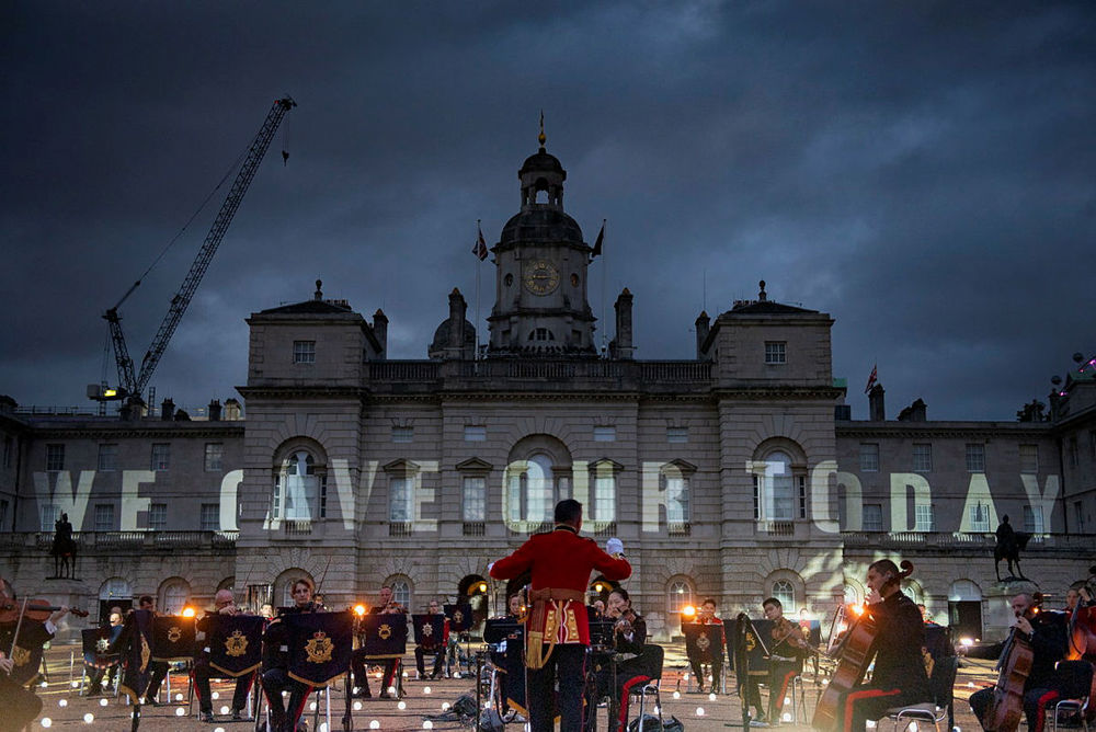 A military band rehearses in front of Somerset House for a VJ Day 75th anniversary concert. The words "WE GAVE OUR TODAY" have been projected in massive letters over the face of the building.