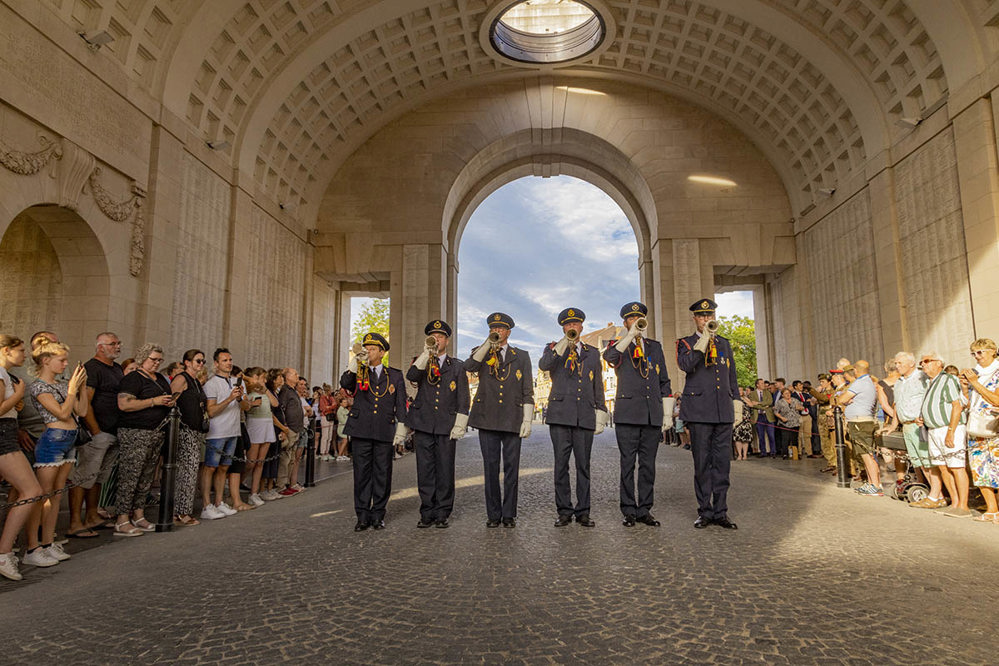 A row of buglers playing beneath the central arch of the Menin Gate, flanked by a crowd of spectators.
