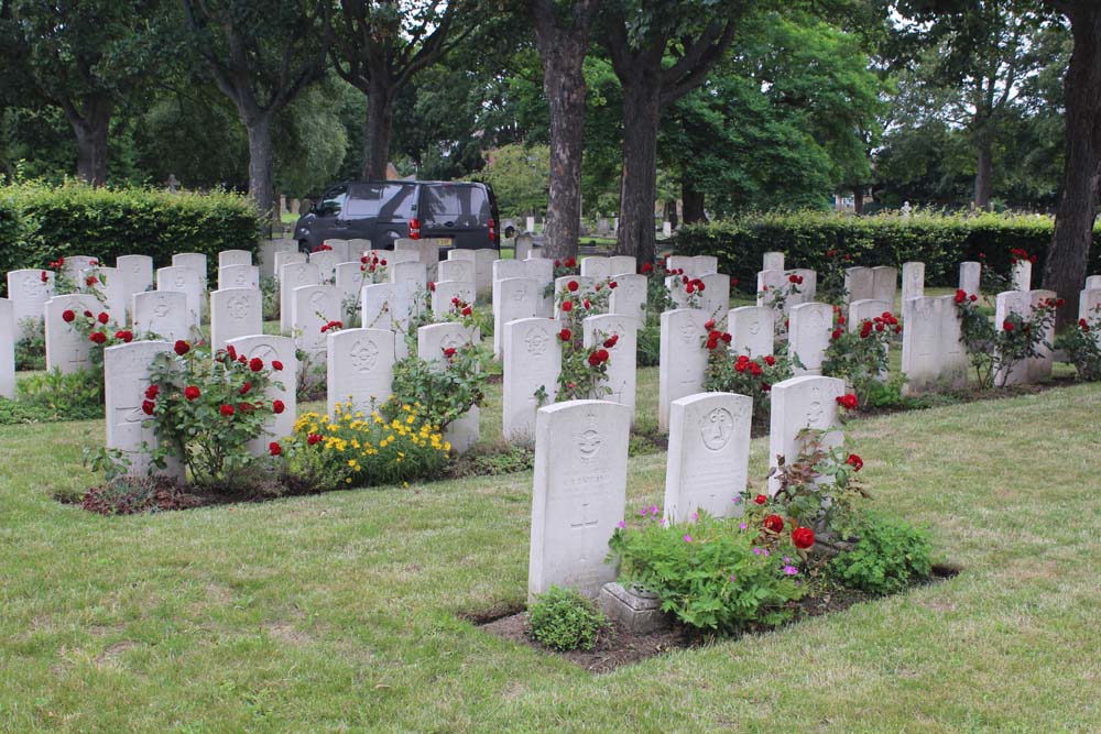 CWGC cemetery showing rows of headstones with extensive red and yellow flowering of the plants in the headstone borders. The lawn has been neatly mowed.