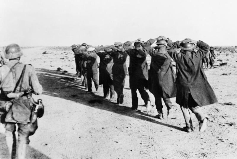 A group of Commonwealth POWs are marched through the North African desert by Wehrmacht soldiers.