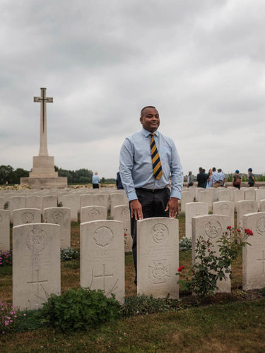 Man poses behind a headstone at Canada Farm cemetery
