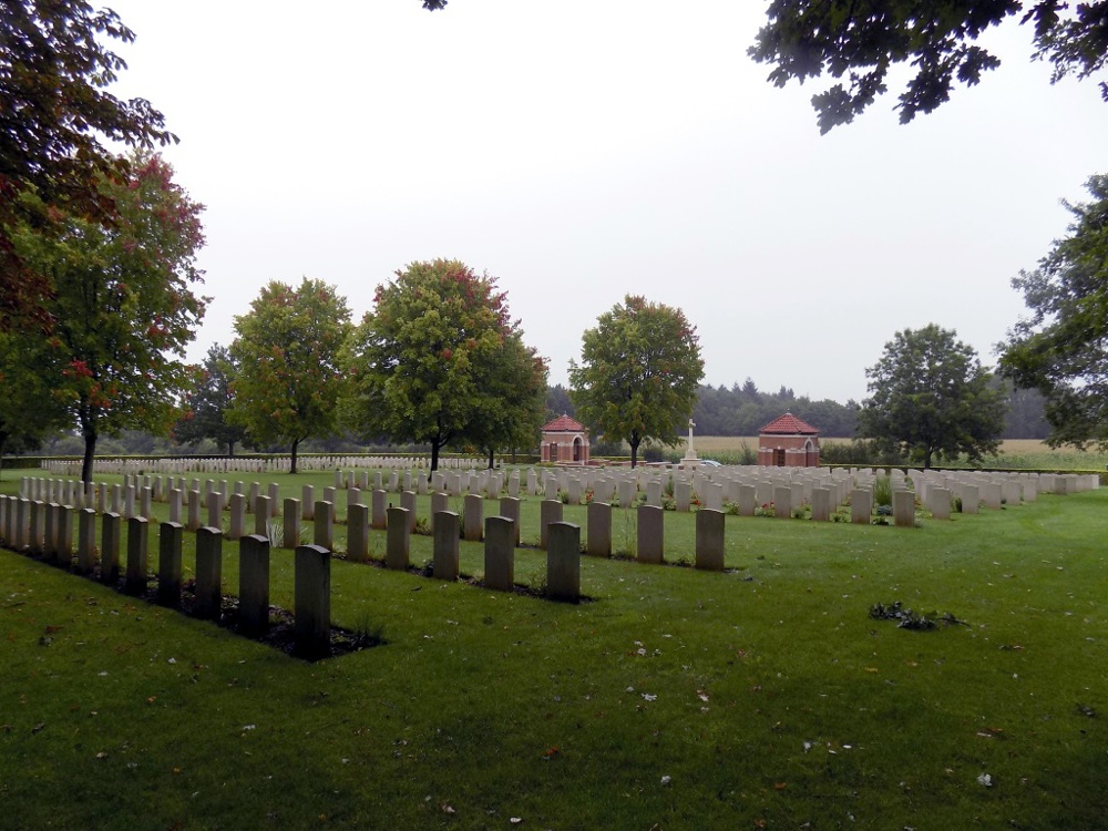 Hotton War Cemetery with headstones, Cross of Sacrifice, and red brick entry pavilions visible.