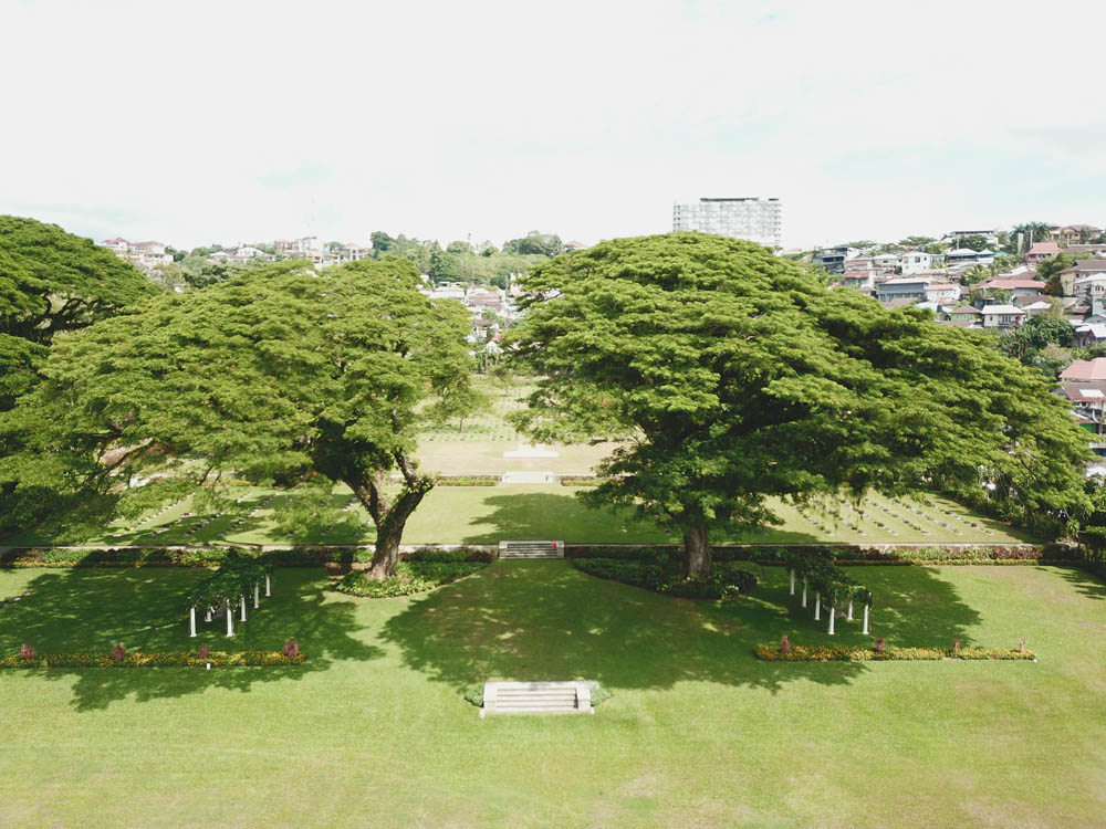 Aerial view of Ambon War Cemetery showing entryway flanked by two giant trees.