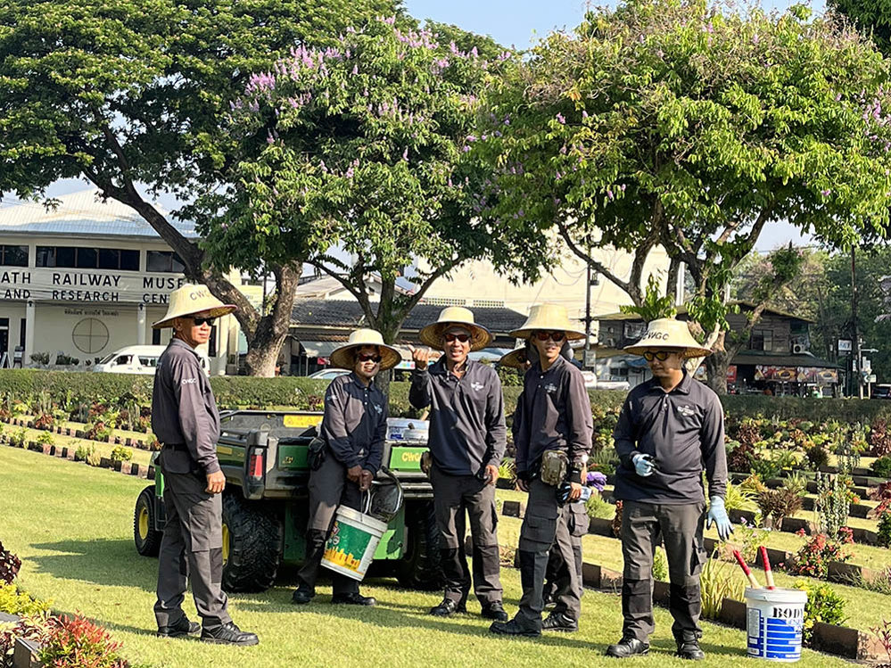 Gardeners posing in sunhats and grey CWGC uniforms at Kanchanaburi War Cemetery