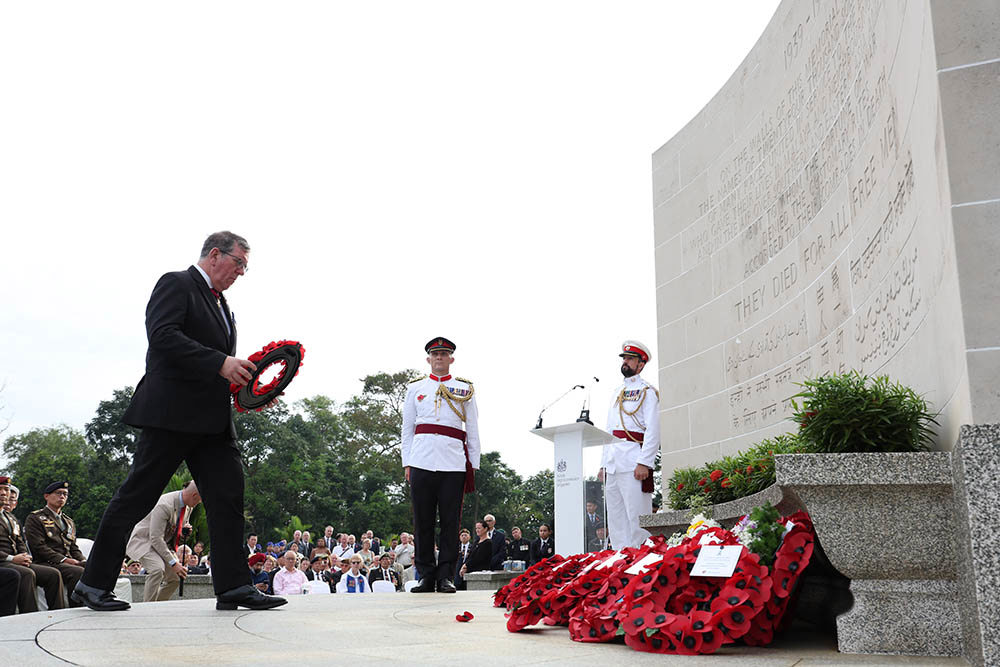A man lays a wreath next to white dress uniformed servicemen on the Kranji Memorial.