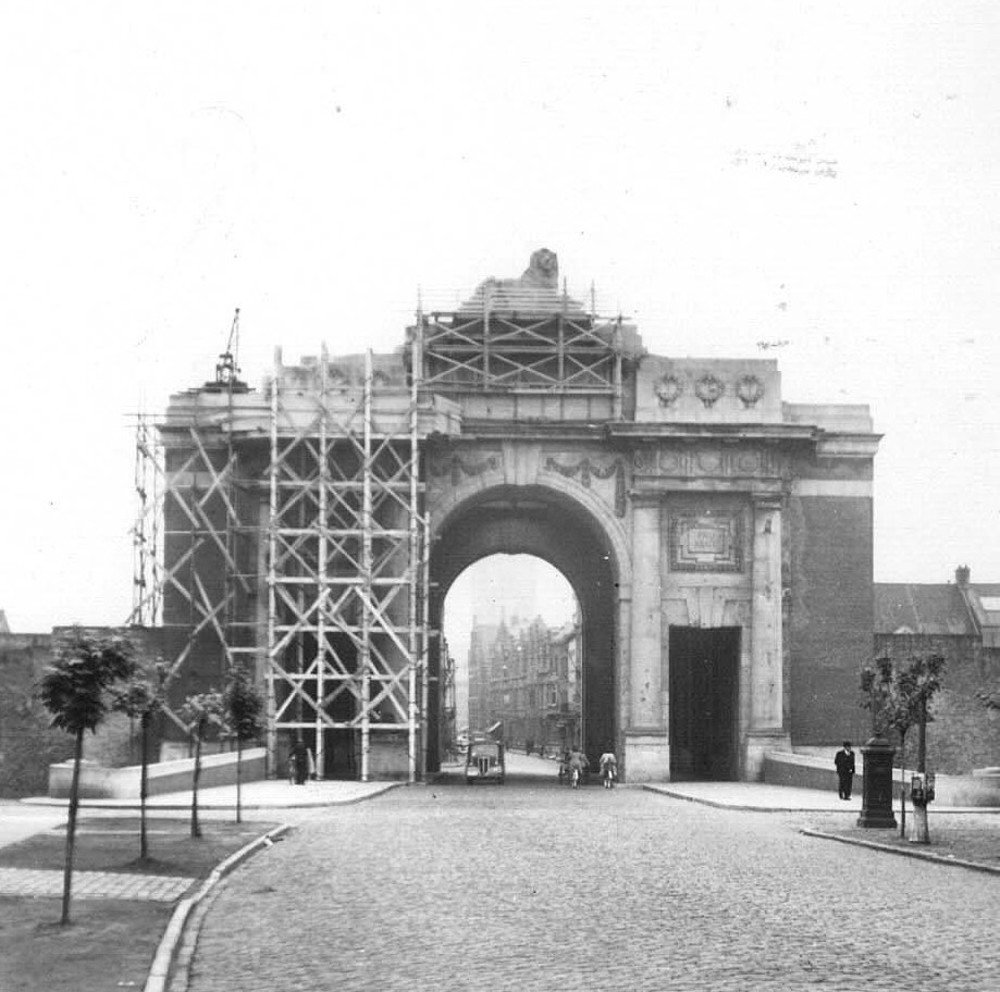 A scaffolding-covered Menin Gate memorial circa 1945 being repaird. A truck is passing through the triumphal arch as are two soldiers on foot.
