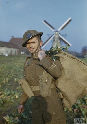 A British soldier poses with a Christmas Sack in front of a windmill.