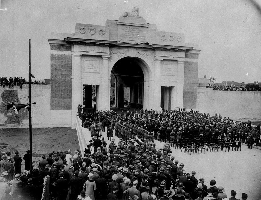 Unveiling ceremony of the Menin Gate. Image shows a large squadron of soldiers standing in formation on the path in front of the arched memorial. A crowd of civilians lines the streets. A loudspeaker is tied to a lamppost to the left of the image.