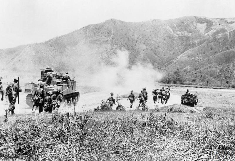 British and Indian soldiers advance along a road towards hills alongside an M3 Lee Tank during the Battle of Imphal.