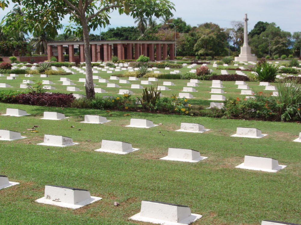 White grave markets stand on a green lawn at Labuan War Cemetery.