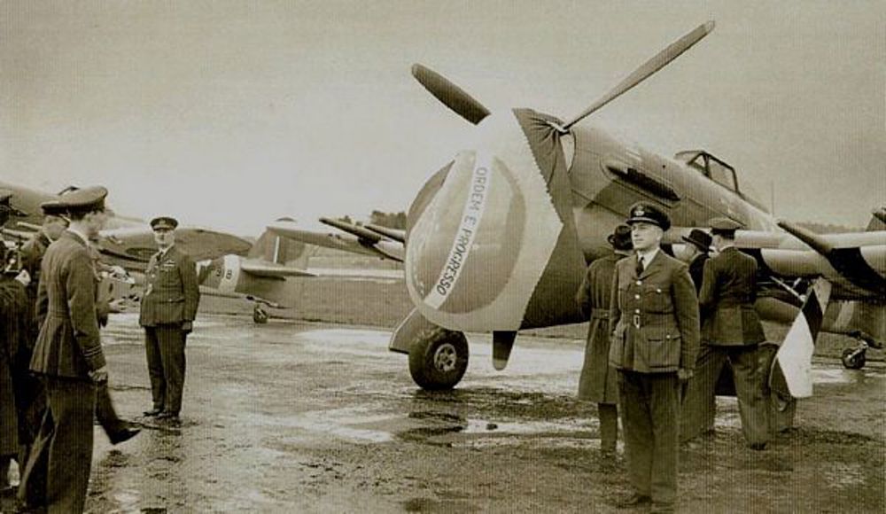 Naming ceremony of a Spitfire used in the BRazilian Squadron, WW2. A large Brazilian flag has been drapped across the aircraft's propellor.