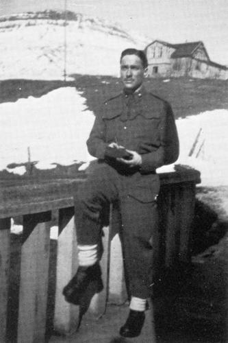 Liuetenant Richard Todd sits on a fence outside a snowbank in Reykjavik, Iceland, in 1942