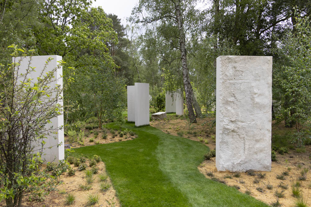 Stone stelae sit beside a grass path beneath a woodland canopy