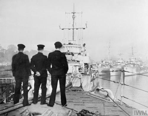 Three sailors look out across numerous destroyers moored alongside each other after returning home to Londonderry from a patrol in the north Atlantic
