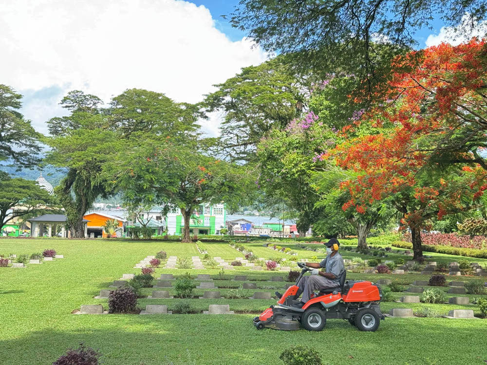 A CWGC staff member on a ride-on lawnmower trims grass at Ambon War Cemetey.