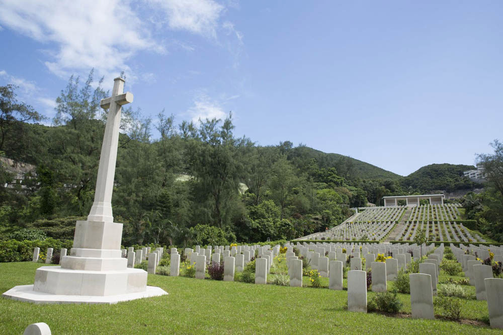 View of Sai Wan War Cemetery taken from the bottom of the hill facing up towards the Sai Wan Memorial. Rows of CWGC headstones run from the base of the hill to the top, just in front of the memorial.