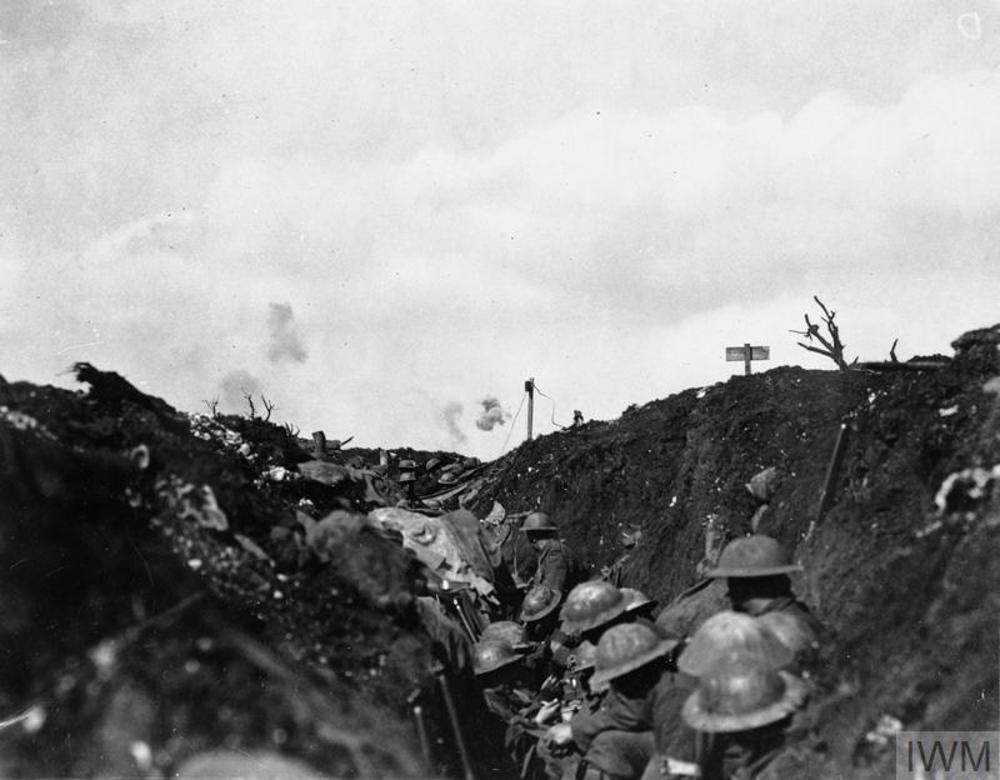 Canadian soldiers taking refuge in a trench during the Battle of the Somme. Plumes of smoke from artillery shells landing nearby are visible in the background.
