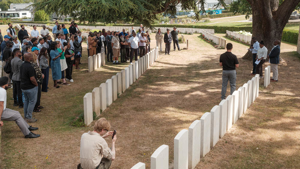 Crowds watch a talk take place amid headstones at a CWGC military cemetery.