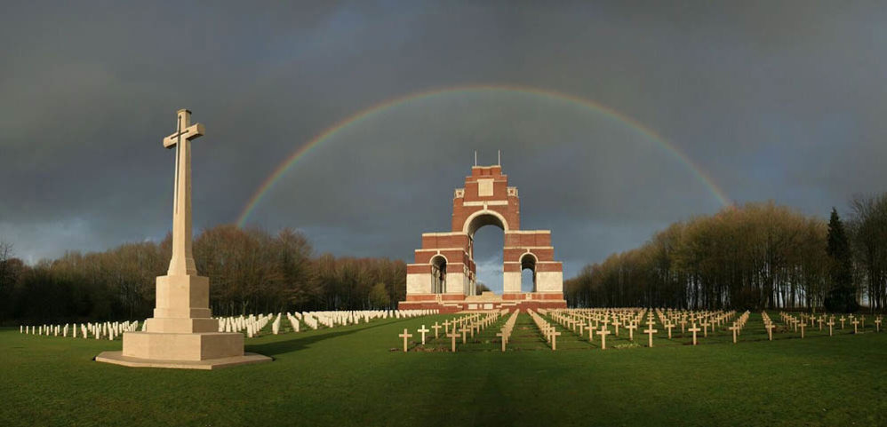 View of the Thiepval Memorial looking ahead from the Cross of Sacrifice from Thiepval Anglo-French Cemetery. A rainbow is breaking over the Thiepval Memorial.
