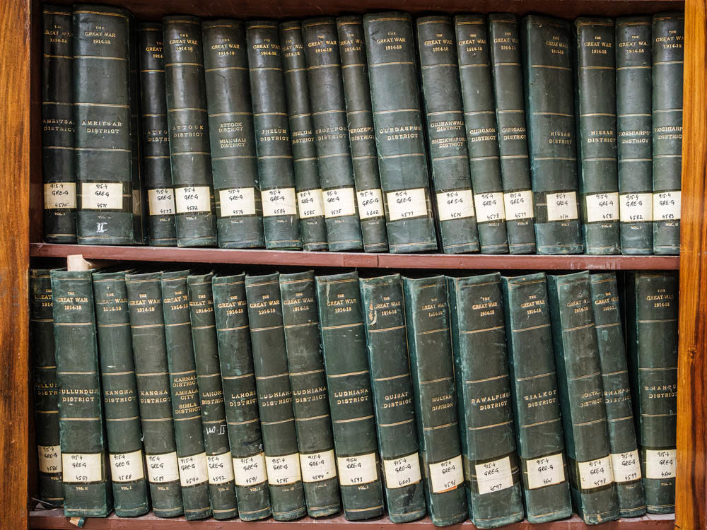 Green leather bound volumes sitting on two shelves of a brown oak wood bookcase.