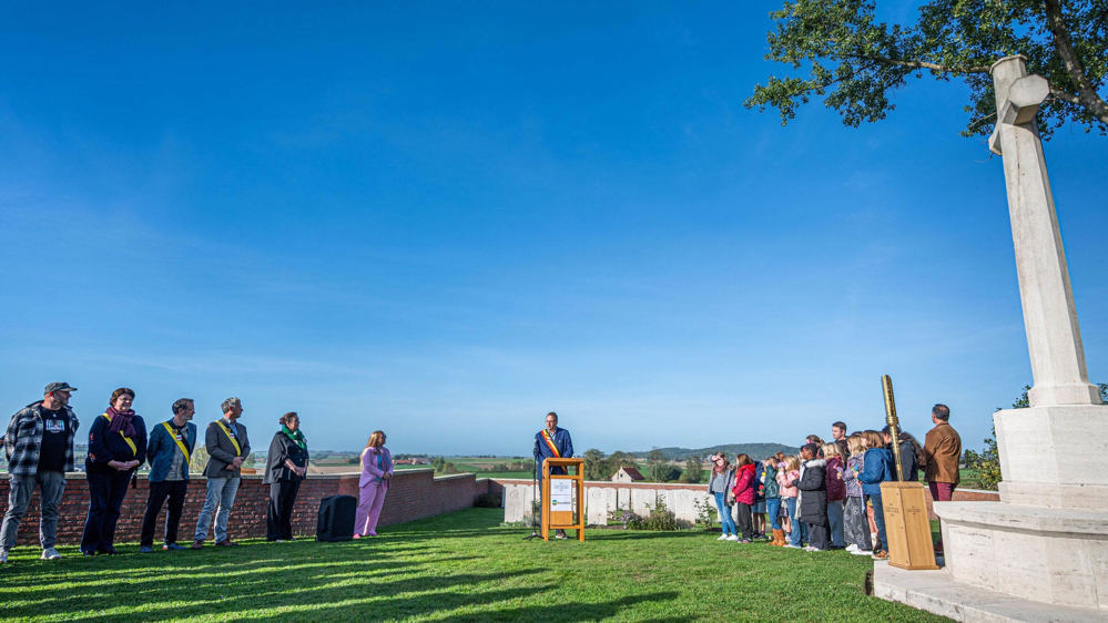Ceremony at Lone Tree Cemetery with a speaker on a rostern addressing a crowd next to the Cross of Sacrifice.