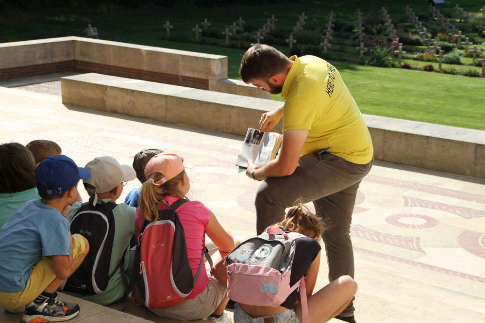 CWGF Guide in a bright yellow polo shirt shows a group of schoolchildren a book on the steps of the Thiepval Memorial.