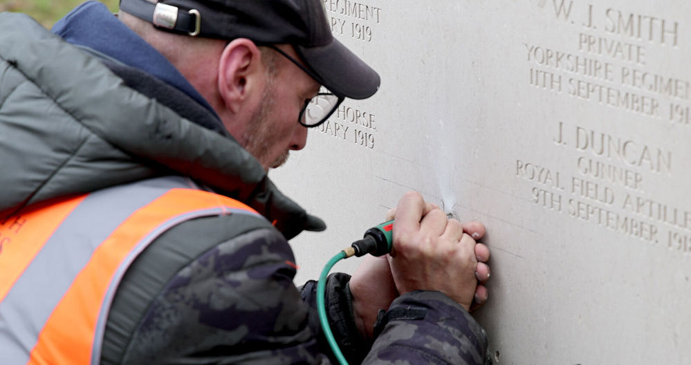 A man in an orange hi-vis vest carves names into a stone stelae at the Brookwood 1914-1918 Memorial.