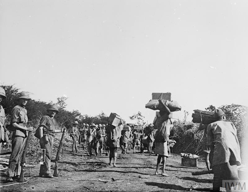 Carriers and labourers hold important supplies while British military officers look on.