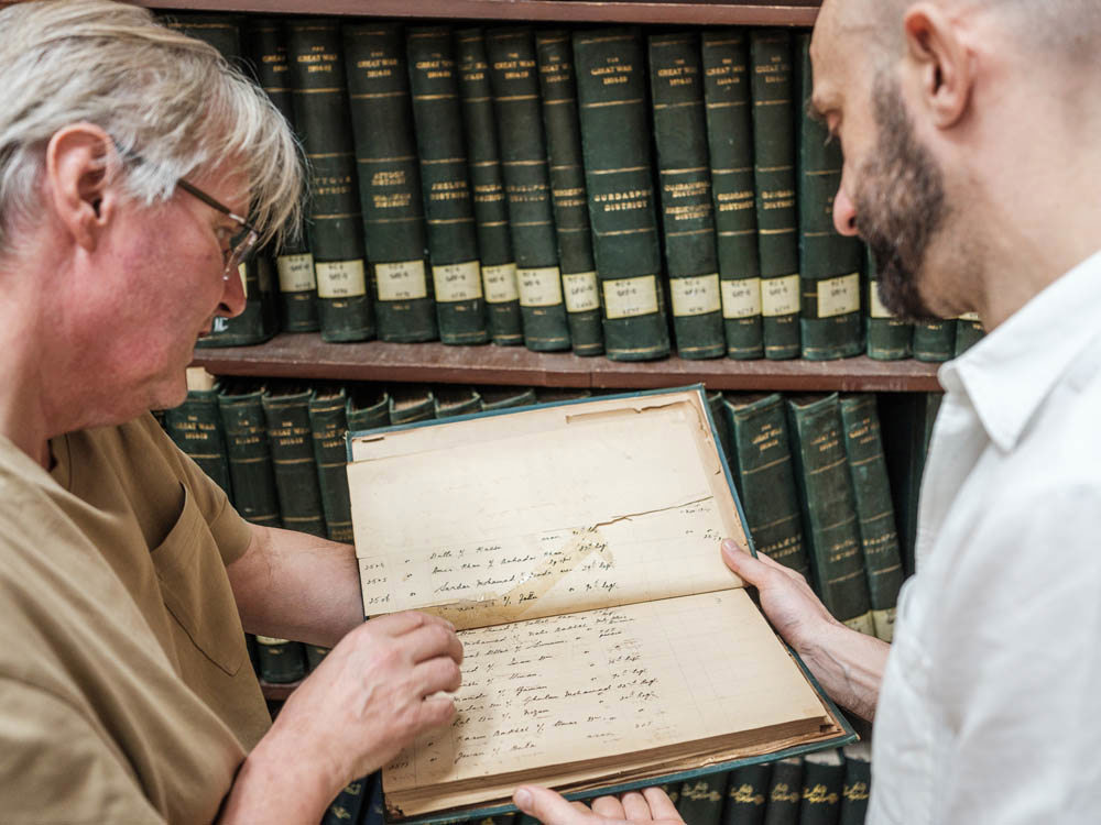 Tow historians inspecting an old book full of yellowed handwritten documents.