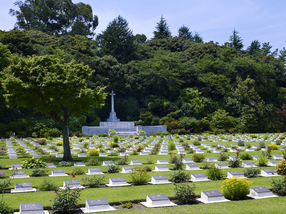 Rows of bronze grave markers marking CWGC war graves head towards the Stone of Remembrance at Yokohama War Cemetery.