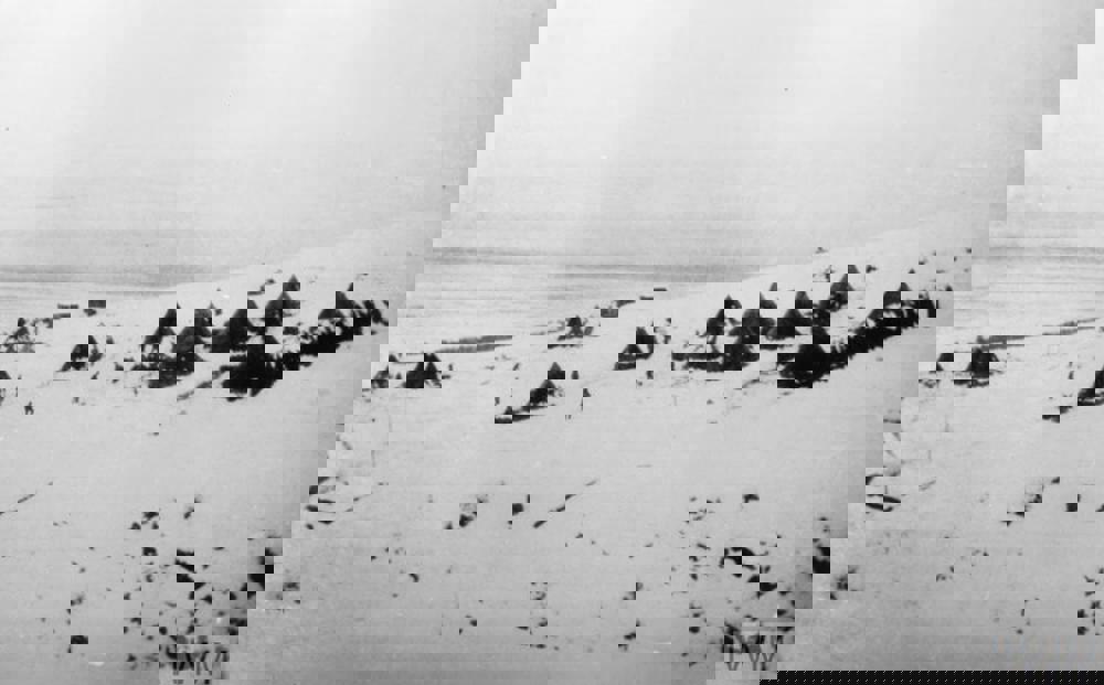 Snow coverd huts and tents of the British Army dot a snow-covered hillside.