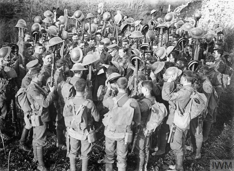 A crowd of WW1 era british soldiers gathered around their officer, reacting jubilantly to the news of the Armistice's signing.