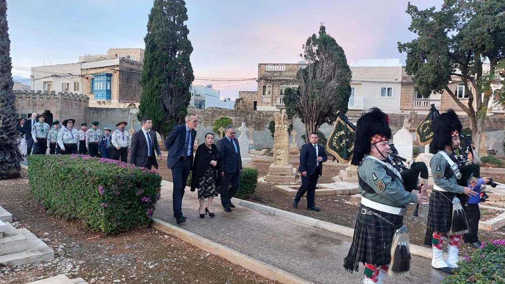 Procession led by two Pipers in kilts passes through a CWGC cemetery in Malta.