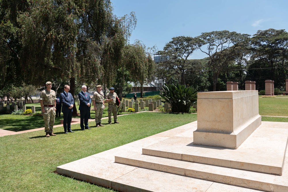 A group of men pays their respects at a Stone of Remembrance in a CWGC cemetery.
