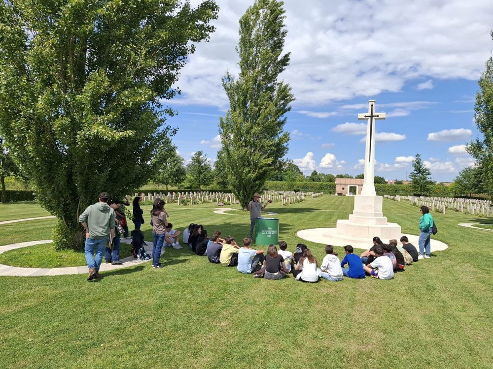 Schoolchildren gather around the Cross of Sacrifice at Faenza War Cemetery to listen to a CWGC guest speaker.