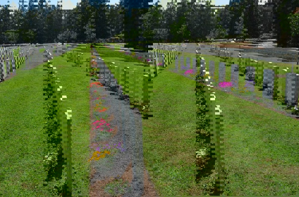 Headstone rows featuring blooming plant borders and a lush green lawn at Ramleh War Cemetery.