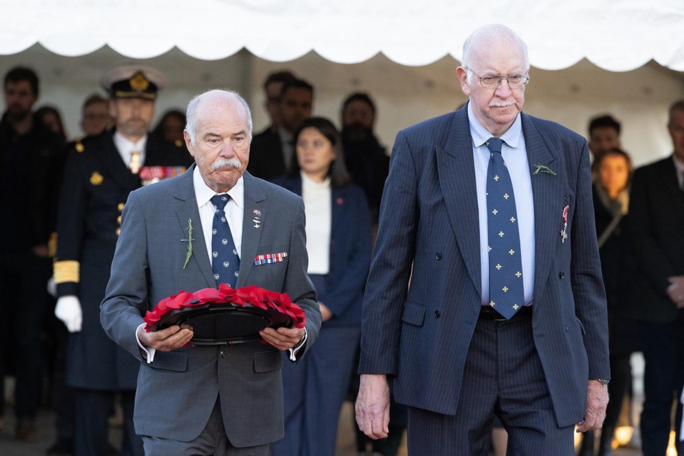 Tow middle aged men holding a poppy wreath.