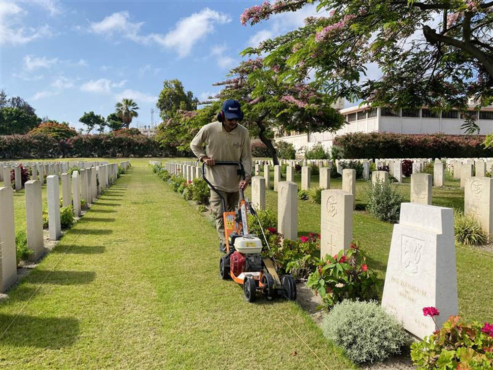 A CWGC gardener trims the lawn and borders at Alexandria (Hadra) War Cemetery with a small lawnmower
