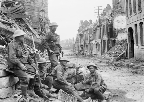 A squad of World War One era Australian soldiers pause for rest amidst the rubble of a shell-hit town street.