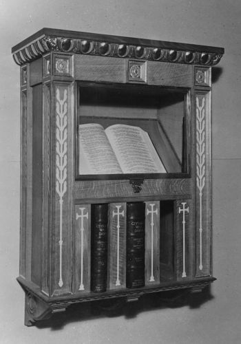 Civilian Roll of Honour in an ornate wooden cabinet. The volumes are seveal leather bound books placed on a shelf with an open volume sat above in a reading cabinet recess.